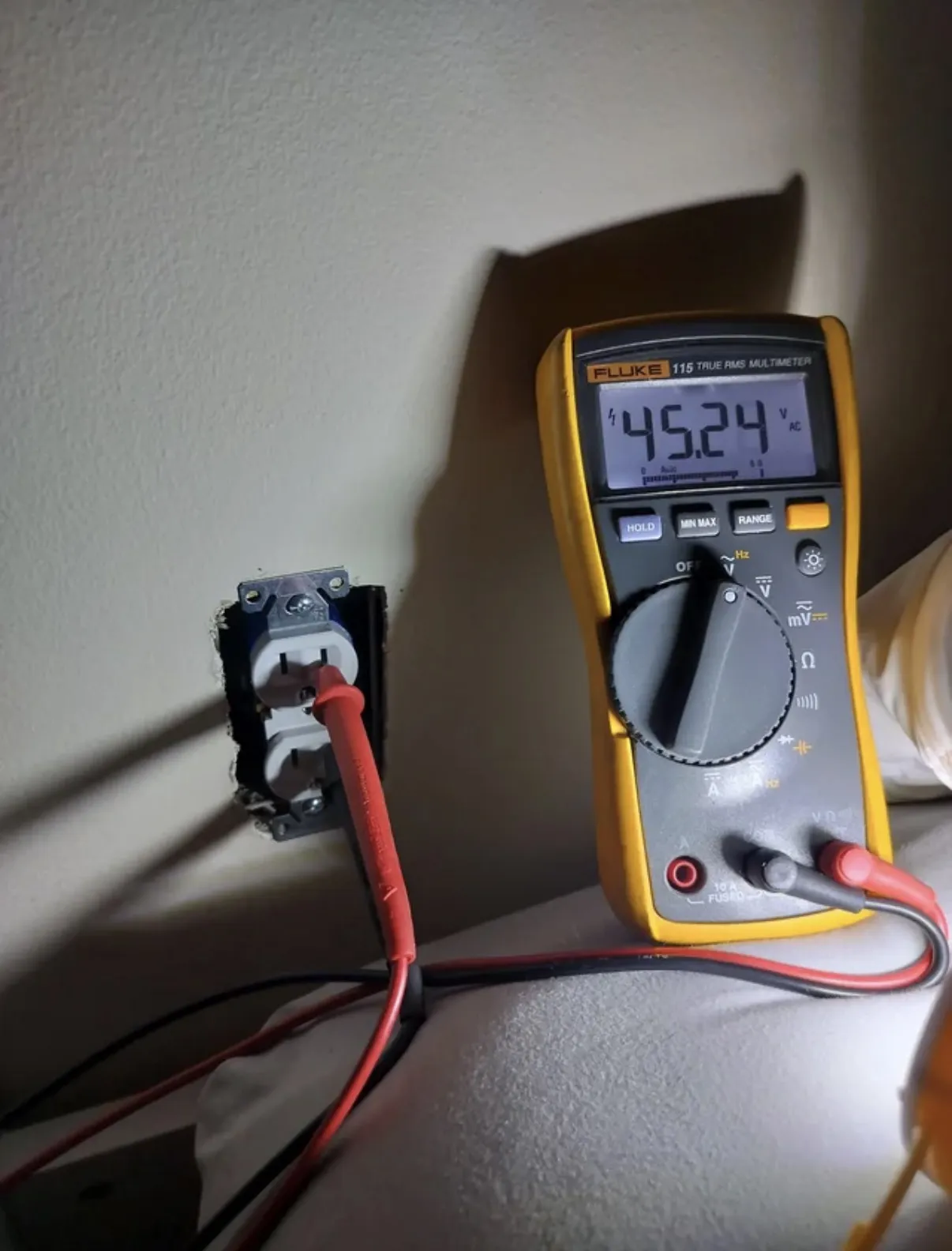 Electrician testing a wall receptacle while troubleshooting a circuit